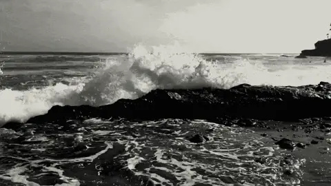Slow-motion monochrome wave crashing near rocks